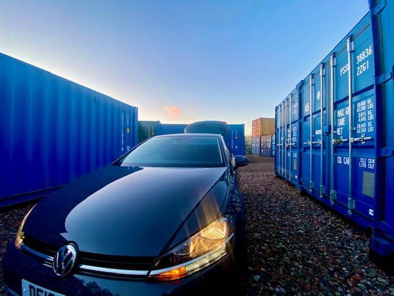motor car driving on to a self storage facility showing floodlit shipping containers